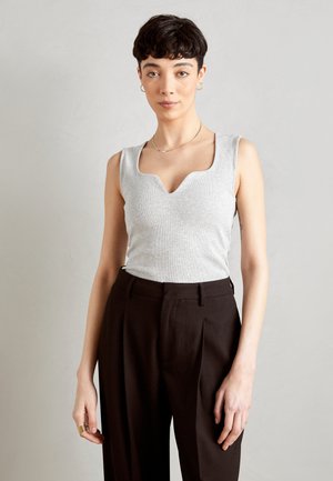 Top de tirantes gris con canalé y escote festoneado, combinado con pantalones marrones de tiro alto con pliegues. Joyería sencilla de oro complementa el atuendo.
