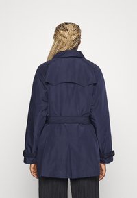 Trench coat blu navy con vita con cintura, spalline con alamari e dettaglio con spacco posteriore. Tessuto liscio e maniche lunghe con polsini regolabili.