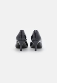 Scarpe con tacco alto in vernice nera, con punta affusolata e tacco curvo, caratterizzate da una finitura liscia e lucida e da un sottile dettaglio di cucitura.