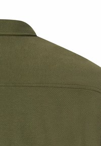 Zielonooliwkowy teksturowany materiał, pokazujący plecy koszuli z kołnierzykiem, z minimalnym detalem przeszycia w pobliżu szwu na ramieniu.