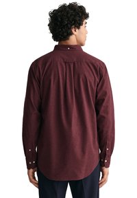 Camisa burdeos de botones con un ajuste relajado, mangas largas con puños de botón y detalle de yugo en la parte posterior. Fabricada con tejido texturizado.