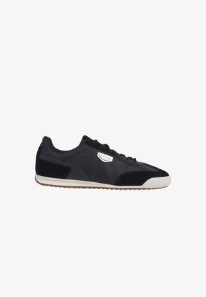 Zwarte lage sneaker met witte rubberen zool, gestructureerde neuskap, vetersluiting aan de voorkant en een klein metalen merkembleem aan de zijkant.