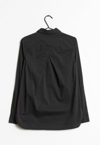 Maglietta nera a maniche lunghe con colletto, caratterizzata da una piega sul retro. Realizzata in un tessuto liscio, presenta dettagli con bottoni sulle maniche.