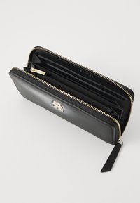 Portafoglio in pelle nera con chiusura zip dorata, multiple fessure per carte e una tasca interna con zip per le monete. Esterno texturizzato e dettaglio del logo.