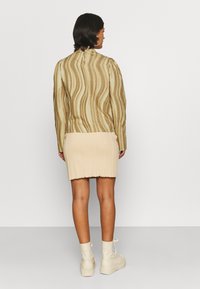 Top de manga longa em bege com padrão ondulado, combinado com uma saia justa creme; tecido texturizado e botas até ao joelho completam o visual.