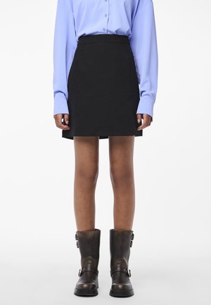 Musta mini-hame, jossa on istuva vyötärö ja suora siluetti. Yhdistetty vaalean sinisen napitettu paita ja ruskeat nilkkurit.