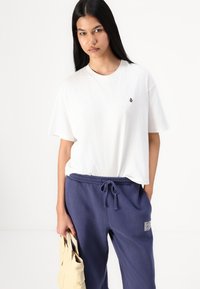 Weißes Baumwoll-T-Shirt mit kurzen Ärmeln und einem kleinen schwarzen Logo. Kombiniert mit navyblauen Sweatpants mit gebundenem Bund und Seitentaschen.