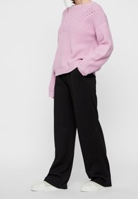 Light pink knitted sweater with ribbed texture and openwork detail, paired with loose black trousers and white sneakers.