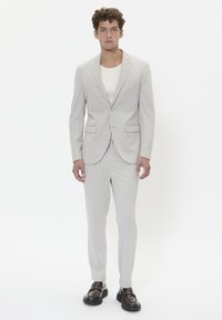 Light gray suit with a single-breasted blazer and matching trousers. Smooth fabric, two front pockets, paired with a white shirt and dark shoes.