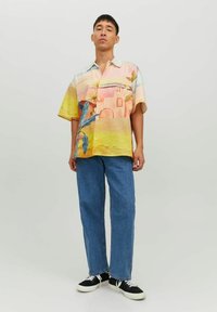 Camicetta a maniche corte con una stampa colorata nei toni del giallo, rosa e blu, che rappresenta foglie tropicali ed elementi architettonici.