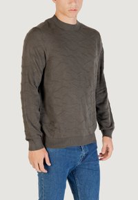 Dunkelgrauer, gestrickter Pullover mit einem strukturierten Wellenmuster, rundem Hals und langen Ärmeln, kombiniert mit blauen Jeans.