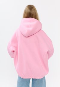 Felpa rosa oversize realizzata in morbido tessuto, con un ampio cappuccio e orlo a coste, abbinata a jeans azzurri strappati.