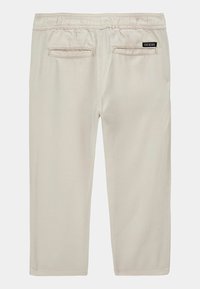 Pantaloni cropped beige con una texture morbida, vita elastica e due tasche posteriori. Presenta un piccolo marchio nero "GUESS" sul retro.