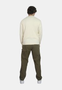 Maglione a maglia crema con bordi a costina, abbinato a pantaloni cargo verde oliva con molte tasche, indossato con sneakers bianche.