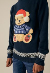 Navy Pullover mit einem Bärenmotiv, der einen blauen Pullover und einen roten Weihnachtsmannhut trägt, mit weißen Akzenten und einem gemusterten Saum. Mit einer gemütlichen Textur gestaltet.