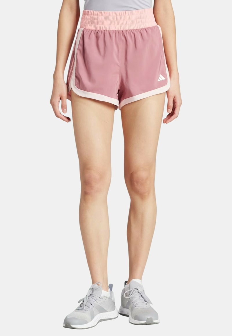 Pantaloni sportivi rosa con una vita elasticizzata arricciata, rifiniture laterali bianche e tessuto leggero, abbinati a sneakers grigie.