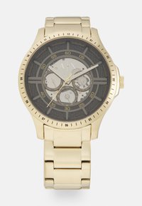 Reloj de acero inoxidable dorado con esfera negra, tres subesferas, acentos texturizados y una pulsera gruesa. Presenta marcadores numerados.