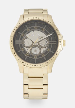 Złoty zegarek ze stali nierdzewnej z czarnym cyferblatem, trzema subcyferblatami, teksturowanymi akcentami i masywną bransoletą. Posiada numeryczne znaczniki.