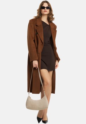 Cappotto di lana marrone con grandi rever, vestito nero, borsa beige, tacchi neri lucidi e occhiali da sole. L'outfit ha un design elegante e moderno.