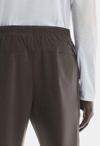 Brown athletic pants with a relaxed fit, elastic waistband, and smooth texture. The top is partially visible, showing a light gray long-sleeve shirt.
