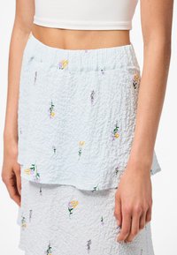 Svetle modrá sukně s mačkanou texturou, květinovou výšivkou v žluté a fialové barvě, vrstvený design a elastický pas.