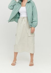 Ljusgrön, huvad jacka med elastiska ärmslut; vit linne; beige, midilång kjol med dragsko och ficka på sidan; nude slide-sandaler.