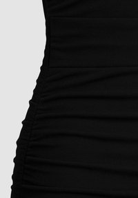 Tessuto nero con dettagli arricciati sul lato, che mostra la trama e le cuciture raccolte, su uno sfondo chiaro e uniforme.