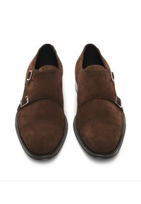 Brown suede double monk strap shoes with silver buckles, pointed toe shape, and black rubber sole. Smooth texture and minimalist design.