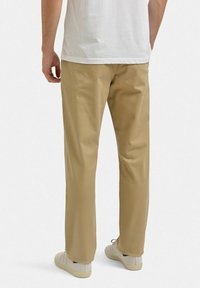 Beige bomuldsbukser med lige snit og en glat tekstur, parret med hvide sneakers. Minimalistisk design, ingen synlige mønstre eller accenter.