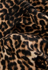 Leopardenmusterstoff mit großen schwarzen und braunen Flecken auf einem beigen Hintergrund, weiche Textur und leicht fallende Optik.