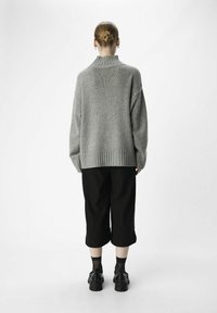 Pull en laine grise avec un col haut à côtes, des manches amples et un ourlet côtelé, associé à un pantalon noir court et des chaussures plateforme.