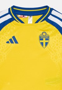 Κίτρινη και μπλε ποδοσφαιρική φανέλα Σουηδίας με το λογότυπο της Adidas, το έμβλημα της ομάδας και διακριτικό floral μοτίβο σ�το μπροστινό μέρος, καθώς και άσπρους ώμους με μπλε ρίγες.