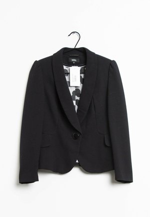 Zwarte damesblazer met enkele knoopsluiting, gestructureerde schouders en een gestippelde voering, hangend aan een zwarte hanger tegen een witte achtergrond.