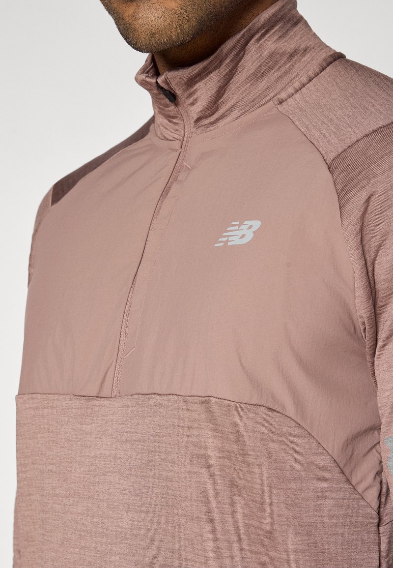 Lyserød, langærmet pullover med lynlås ved halsen. Har en blanding af glat og struktureret stof. Sølvlogo på brystet.