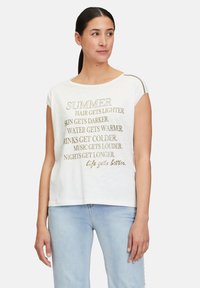 T-shirt blanc à manches courtes avec du texte doré comportant des phrases liées à l'été. Tissu doux, coupe décontractée et accents métalliques discrets sur les épaules.