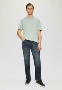 T-shirt vert clair à manches courtes associé à un jean bleu foncé. L'ensemble est complété par des baskets noires à semelles blanches.