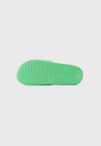 Green rubber sole of a slide sandal with textured grid pattern and embossed logo in the center, shown against a white background.