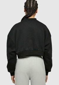Felpa nera corta con collo rotondo, veste larga e orlo a costine. Presenta spalle cadute e tessuto morbido e dalla texture interessante. Abbinata a pantaloni grigi chiari.
