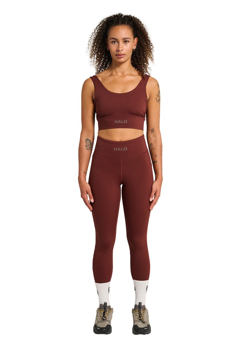 Burgundy idrotts crop top och hög midja leggings-set, med mjukt tyg och HALO-logotypdetaljer. Modellen bär vita strumpor och bruna skor.