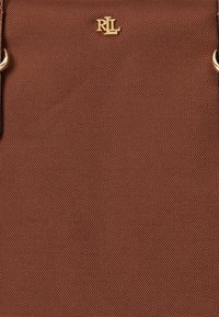 Καφέ τσάντα ώμου με υφή, κατασκευασμένη από ανθεκτικό υλικό, με χρυσές λεπτομέρειες στο λογότυπο και στα αξεσουάρ. Απλός και λειτουργικός σχεδιασμός.