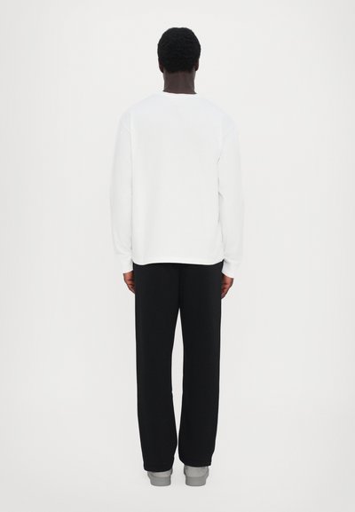 Valgest sweatshirtist, millel on ümara kaelaava ja pikad varrukad. Mustad püksid, millel on lõdvestatud istuvus ja hallid mansetid. Minimalistlik disain, ilma mustriteta.