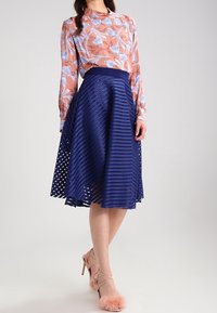 Blommönstrad, genomskinlig ljusrosa blus med långa ärmar, tillsammans med en knä-lång, marinblå, texturerad kjol med utskärningar.