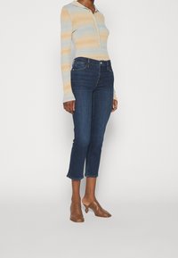 Camisa de manga larga a rayas en azul claro y beige con cuello y botones, combinada con jeans recortados de mezclilla oscura y zuecos de tacón marrón.