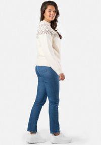 Witte gebreide trui met een patroon aan de schouders, gecombineerd met blauwe jeans en witte sneakers. De trui heeft een losse pasvorm en een ronde hals.