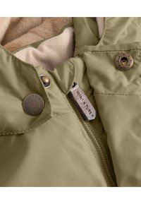 Veste rembourrée verte avec une douce doublure beige, équipée de boutons-pression, d'une fermeture éclair et d'une étiquette cousue dans le col.