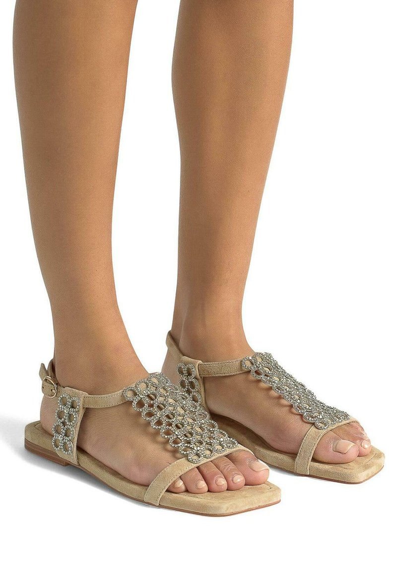 Infradito beige con suola piatta, dotate di una fascia decorativa di perline sulla parte superiore del piede e chiusura a fibbia alla caviglia. Materiale in morbido camoscio.