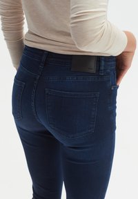 Dunkelblaue Jeans aus Denim mit einer taillierten Passform, ausgestattet mit zwei Gesäßtaschen und einem schwarzen Lederpatch am Bund.