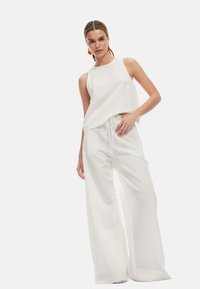 Top bianco senza maniche con vestibilità ampia, abbinato a pantaloni bianchi a gamba larga con vita regolabile. Tessuto morbido e design minimalista.