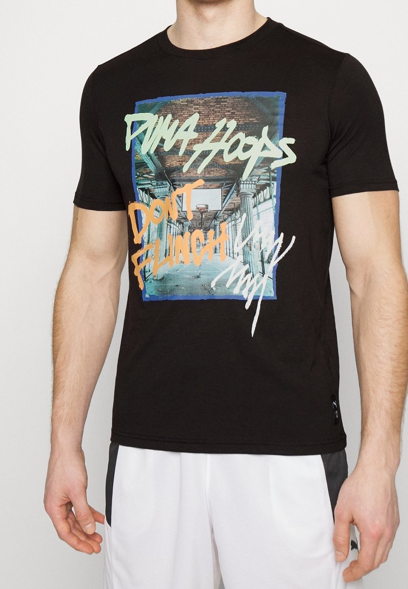 Camiseta de algodón negra con un diseño gráfico que presenta "PUMA HOOPS" y "DON'T FLINCH", resaltado en colores como verde, naranja y blanco.