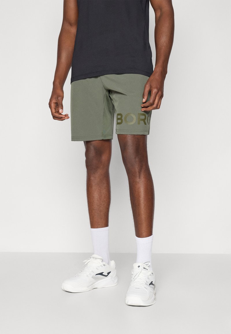 Grønne sportsshortser med "BORO" trykket med fet skrift, avslappet passform, flat midje, og kombinert med hvite joggesko og ankelstrømper.
